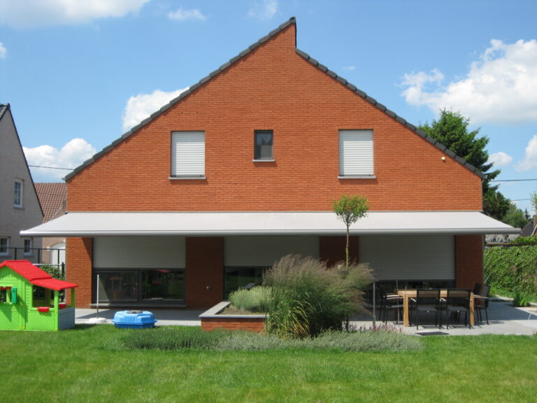 Groot knikarmscherm uitgeklapt boven het terras van een bakstenen woning